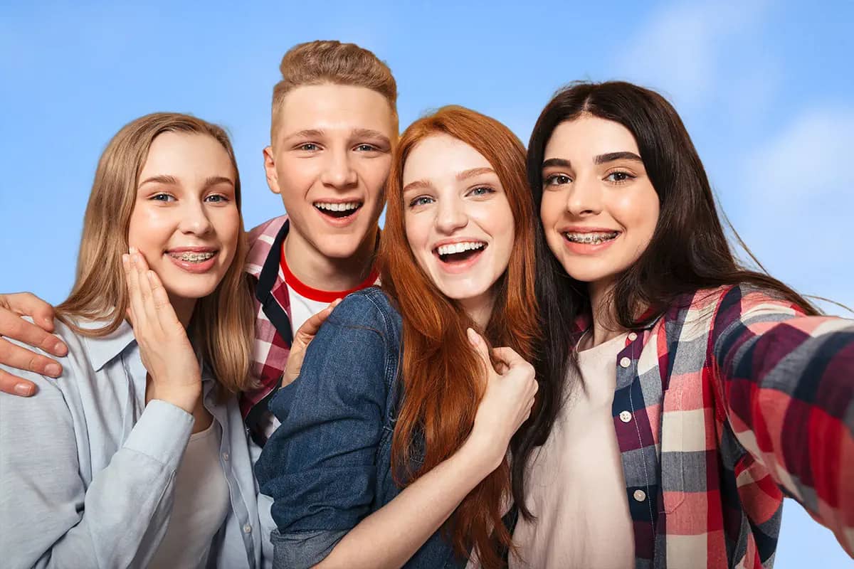 group of four smiling teens taking selfie